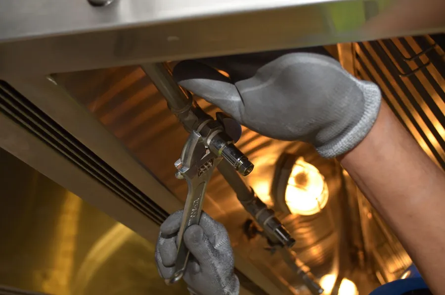 Gloved hands using a wrench on a pipe connection